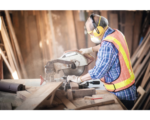 Hantverkare med cirkelsåg som sågar trä med personlig skyddsutrustning i en verkstad.