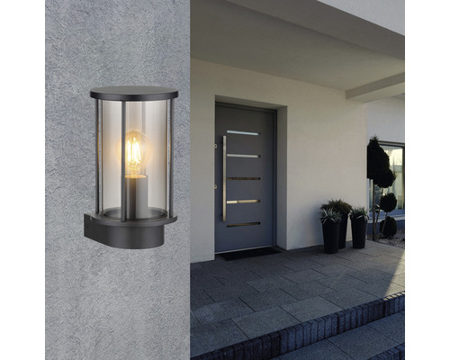 En svart vägglampa med klart glas på en husvägg bredvid en ytterdörr.