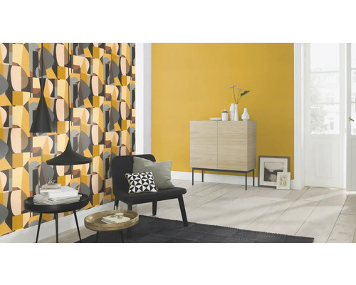 Vardagsrum med mönstrad tapet, byrå och fåtölj.