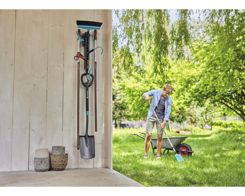 Trädgårdsscen med verktygshållare, trädgårdsredskap och person som arbetar i trädgården