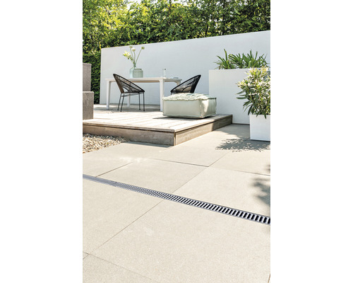 Terrass med dräneringsränna, bord, stolar, växter och sittpuff