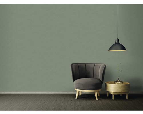 Inredningsexempel med fåtölj, sidobord och pendellampa framför en grön vägg