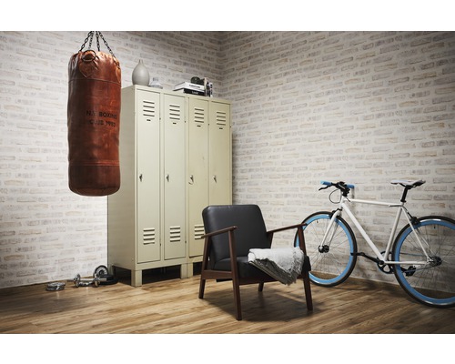 Scen med boxningssäck, skåp, fåtölj, cykel och hantlar i ett rum med tegelvägg