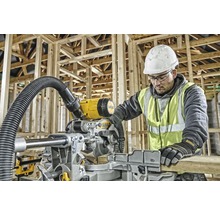 En man med skyddshjälm och varselväst använder en DeWalt kap- och geringssåg i en råkonstruktion.