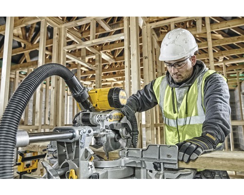En man med skyddshjälm och varselväst använder en DeWalt kap- och geringssåg i en råkonstruktion.
