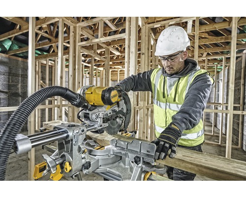 En arbetare använder en DeWalt geringssåg på en byggarbetsplats för att såga en träplanka.