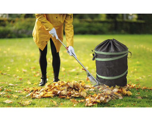 Kvinna som samlar löv med en kratta och en trädgårdssäck