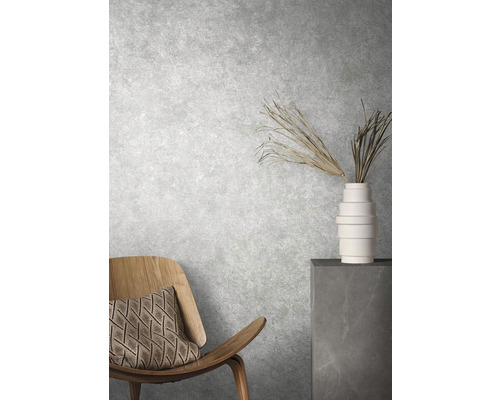 Dekorativ interiör med stol, kudde, vas och prydnadsväxter framför en strukturerad vägg