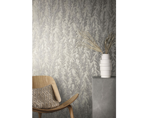Rumsöversikt med strukturtapet med växtmönster, en träfåtölj och en vit vas.