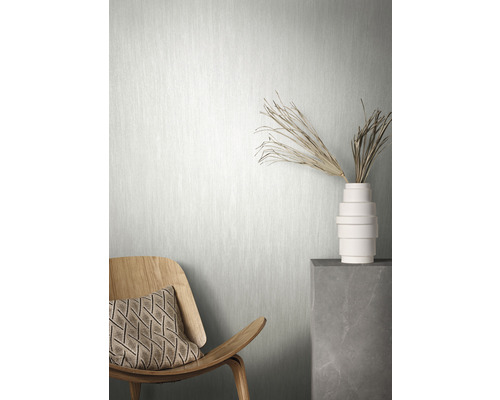 Miljöbild med en ljus non-woven tapet, en trästol med dyna och en vas med dekoration på en sockel