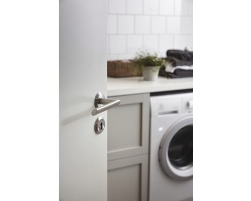 Öppen dörr med dörrhandtag i en tvättstuga med tvättmaskin, hylla, växt och hopfälld tvätt.