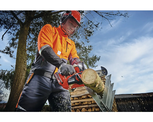 En person med skyddskläder sågar en träbit på en sågbock med en batteridriven motorsåg.