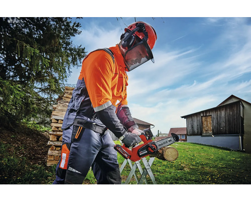 Person med skyddshjälm och hörselskydd arbetar med en batteridriven motorsåg utomhus.