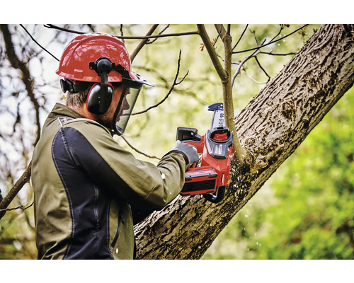 Man med skyddshjälm och batteridriven motorsåg beskär trädgrenar