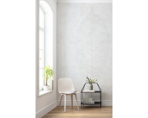 Ljust rum med stol, sidobord, växt och väggdekal med bladmotiv