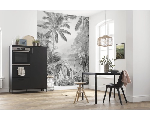 Matsal med svart matbord, stol och skänk framför en fototapet med djungelmotiv.