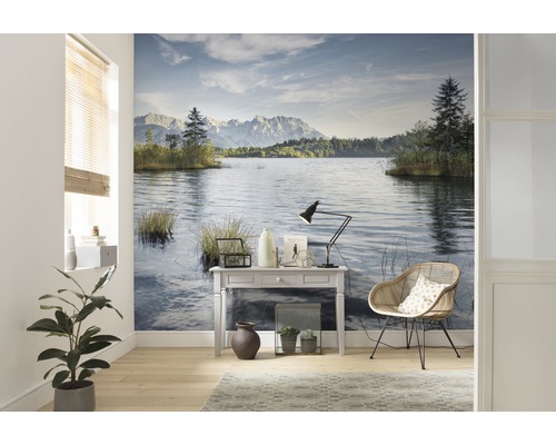 Vardagsrum med en fotovägg som visar en sjö och berg, samt ett bord, en lampa och en stol.