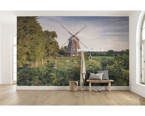 Väggmålning med en väderkvarn, får och frodig grönska i ett ljust rum.