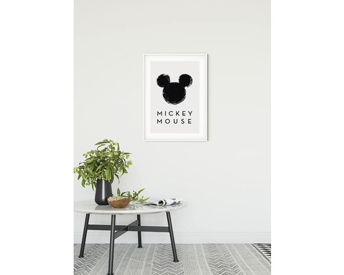 Dekorativ inramad bild med Mickey Mouse-motiv ovanför ett bord med vas och skål