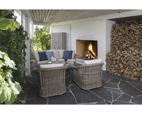 Veranda med rottingfåtöljer, soffa, soffbord, öppen spis och vedstapel