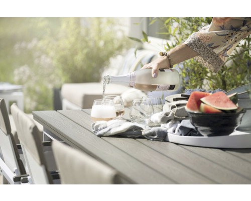 Scen med mousserande vin som hälls upp i glas på ett trädgårdsbord, med stolar och vattenmelon
