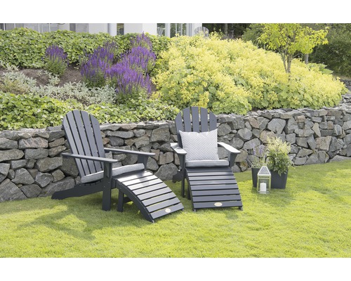 Två Adirondack trädgårdsstolar med fotstöd på en gräsmatta framför en stenmur