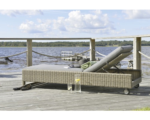 Vadderad trädgårdsliggstol i rotting på en träterrass med utsikt över sjön