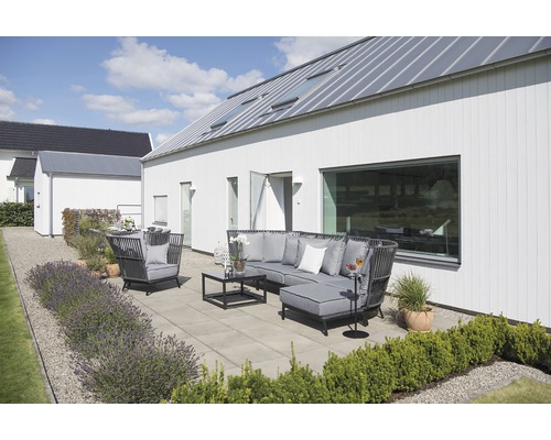 Trädgårdsscen med loungeset, fåtölj och bord på en terrass intill ett modernt hus