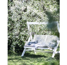 Vit trädgårdsswing med kuddar och filt under ett blommande träd