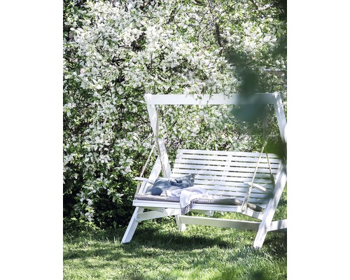 Vit trädgårdsswing med kuddar och filt under ett blommande träd