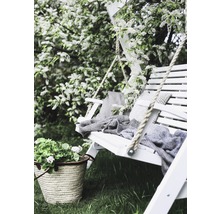 Trädgårdsscen med vit gunga, kuddar, filt, blommor och korg i trädgården