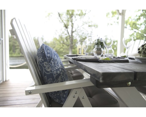 Detaljvy av ett trädgårdsbord med stol och mönstrad kudde på en terrass.
