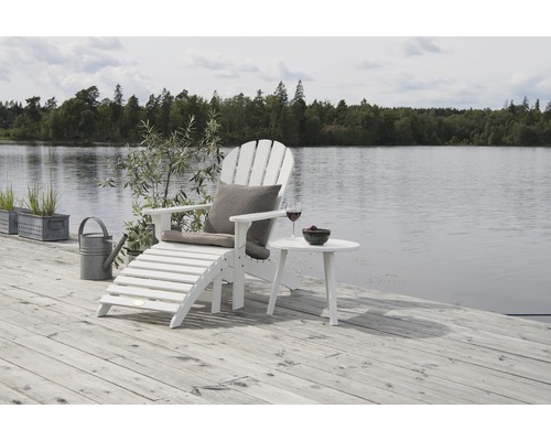 Scen med en vit Adirondack-stol med fotstöd, kuddar och sidobord vid sjön