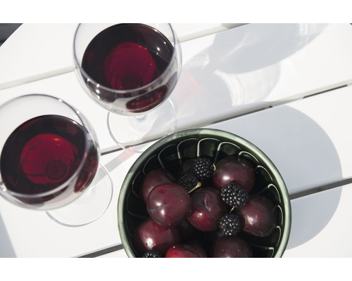 Två vinglas med rött vin och en skål med plommon och björnbär på ett bord