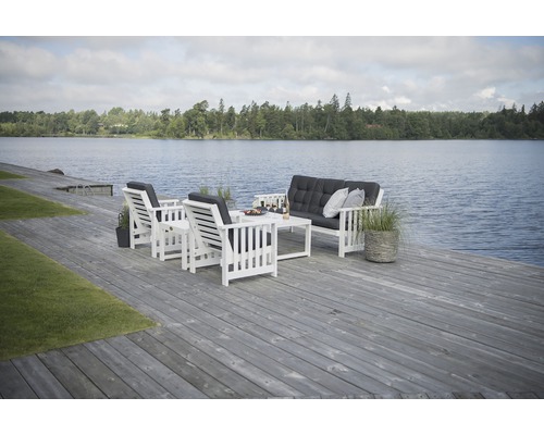 Trädgårdsmöbler med soffa, fåtöljer och bord på träterrass vid sjön