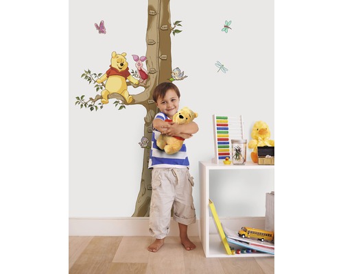 Pojke kramar Winnie the Pooh gosedjur framför en vägg med Winnie the Pooh väggdekal och tillväxtskala.