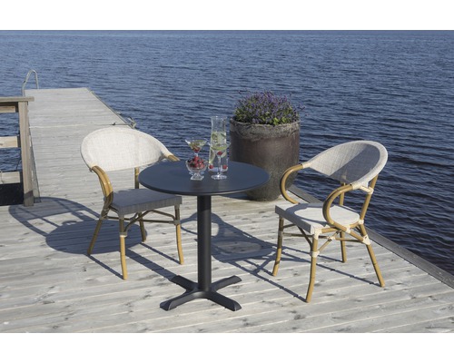 Trädgårdsscen med bord och två rottingstolar på en träterrass vid sjön.