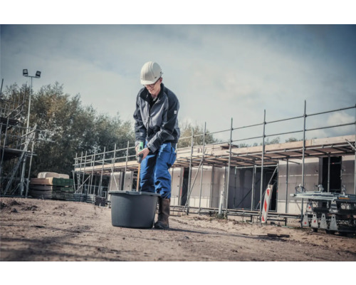 Byggnadsarbetare blandar material i en hink med en omrörare på en byggarbetsplats.