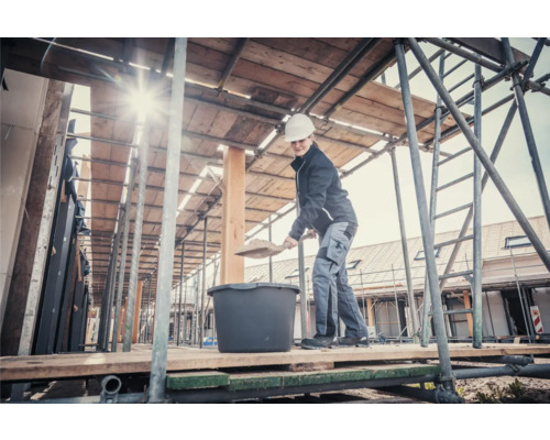 Kvinna med spade och murbruksbalja på en byggnadsställning