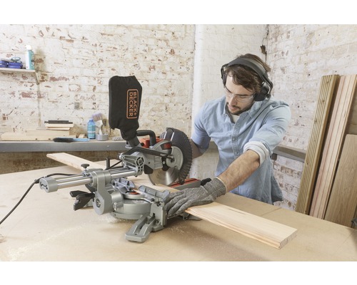 Man med hörselskydd och skyddsglasögon arbetar med en Black and Decker kap- och geringssåg på ett arbetsstycke.