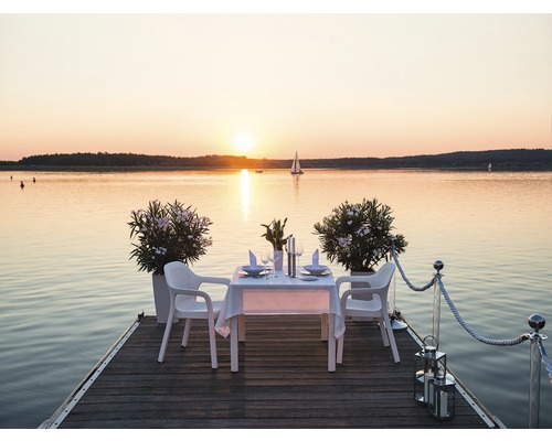 Ett dukat bord med stolar på en träbrygga med utsikt över en sjö i solnedgången.