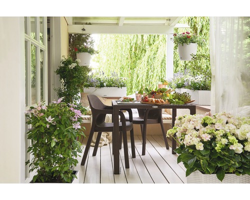 Ljus veranda med matbord, stolar, blomlådor och hängande blomkrukor.