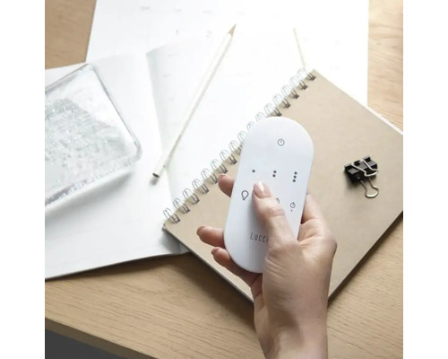 En hand håller en Lucci fjärrkontroll över en anteckningsbok.