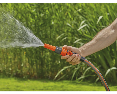 En person håller en trädgårdsslang med sprutmunstycke som det kommer vatten ur.