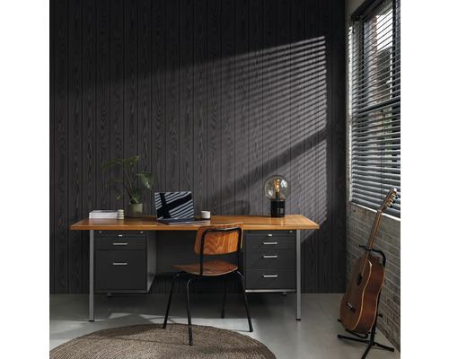 Kontor med skrivbord, stol, lampa, gitarr och bärbar dator framför en mörk träpanel