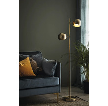 Golvlampa med två lampskärmar bredvid en soffa och en krukväxt