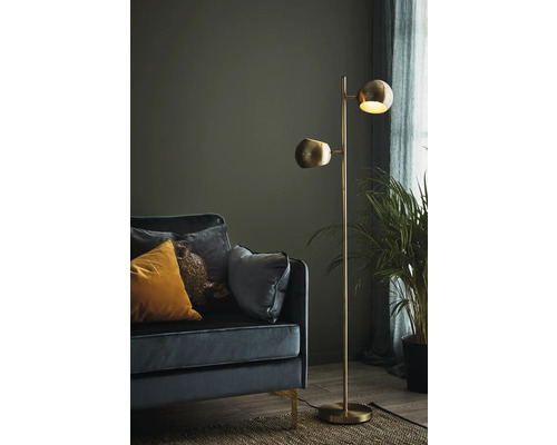 Golvlampa med två lampskärmar bredvid en soffa och en krukväxt