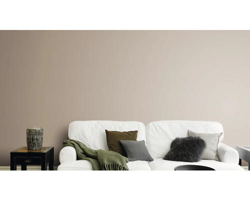 Vardagsrum med vit soffa, kuddar, filt och dekorativ vas på ett sidobord framför en enfärgad vägg