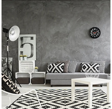 Vardagsrum med grå vägg, soffa med kuddar, matta med geometriskt mönster och vitt soffbord.