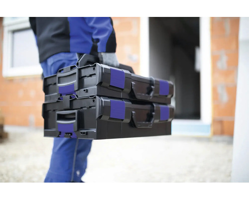 Hantverkare bär två svarta verktygslådor på en byggarbetsplats